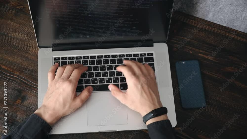 a male programmer in a black shirt is working at a laptop, close-up of the program code and developer's hands on a laptop. modern young programmer sitting at a wooden table at a computer a male programmer in a black shirt is working at a laptop, close-up of the program code and developer's hands on a laptop. modern young programmer sitting at a wooden table at a computer