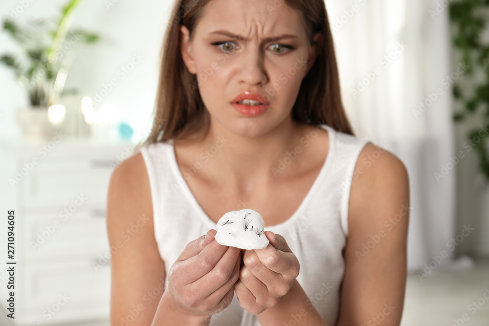 Emotional young woman holding cotton pad with fallen eyelashes indoors Emotional young woman holding cotton pad with fallen eyelashes indoors