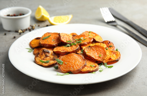 Plate with baked sweet potato slices on grey table, closeup