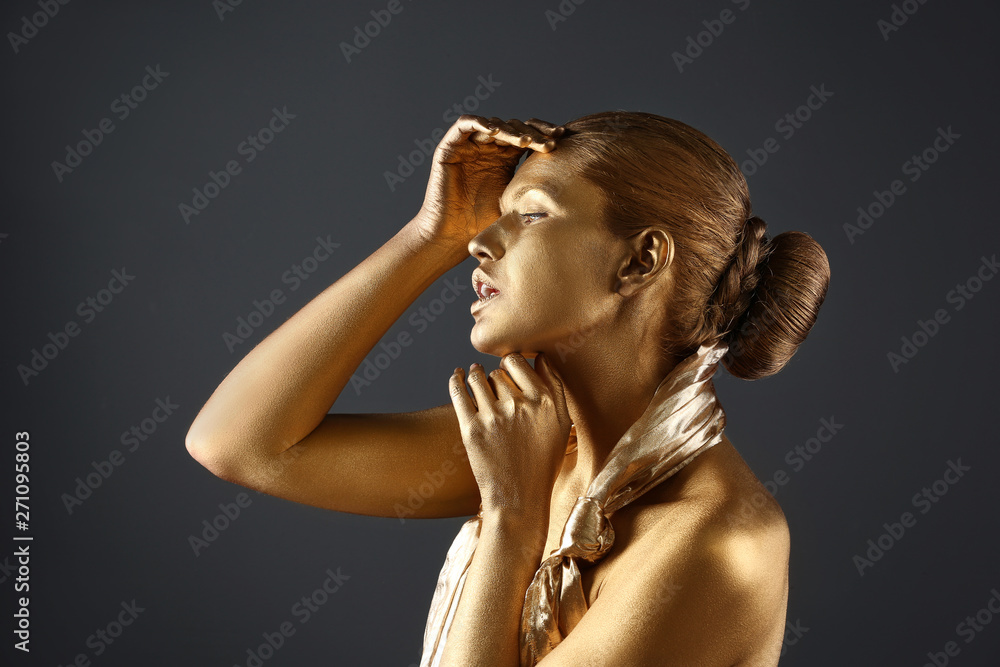 Fototapeta premium Portrait of beautiful lady with gold paint on skin against grey background