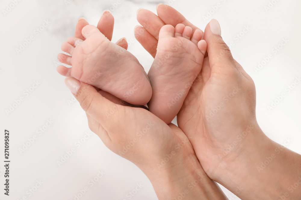 Mother holding baby's feet on light background, closeup Mother holding baby's feet on light background, closeup