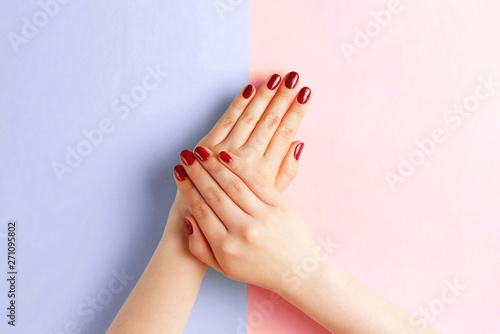 Female hands with red manicure on a pink and blue background, top view