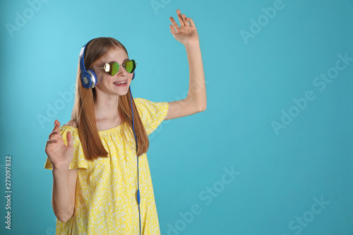 Teenage girl enjoying music in headphones on color background. Space for text