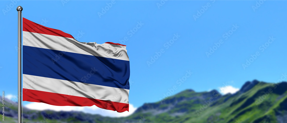 Obraz premium Thailand flag waving in the blue sky with green fields at mountain peak background. Nature theme.