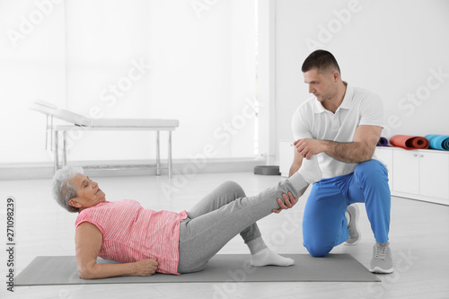 Professional physiotherapist working with elderly patient in rehabilitation center. Space for text