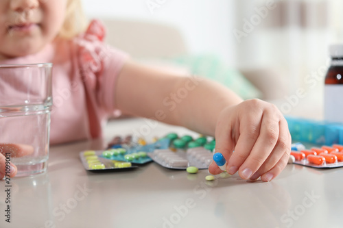 Little child with many different pills and water at table indoors, closeup. Danger of medicament intoxication