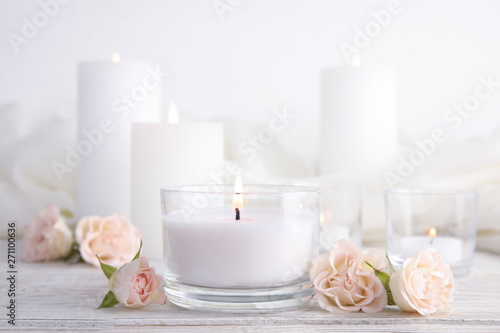 Composition with burning aromatic candle and roses on wooden table