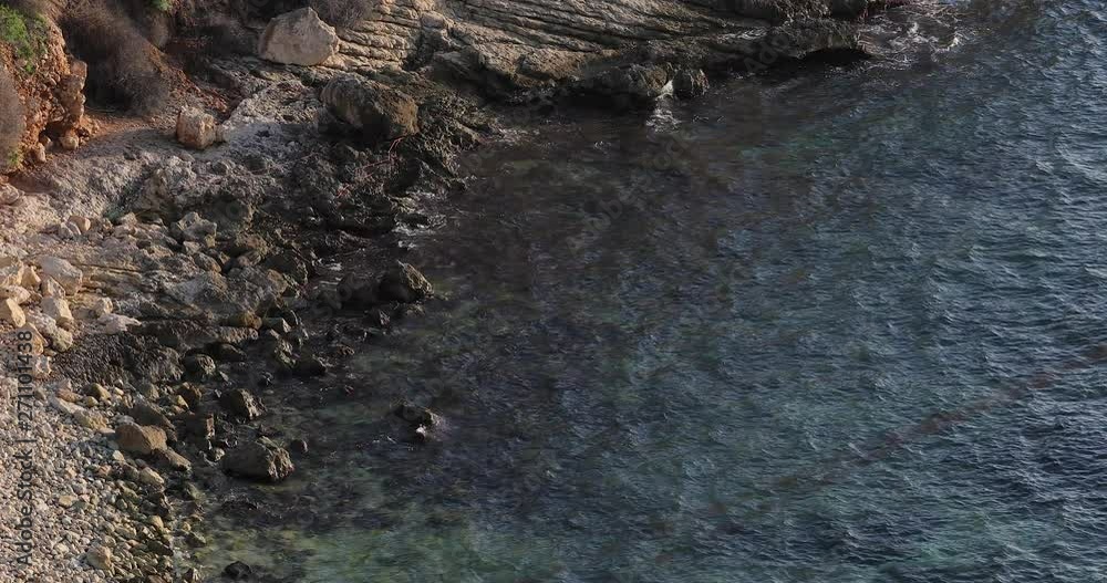View above rocky pebble coastline shore. Deep turquoise, clear waves washing over colorful stones. View above rocky pebble coastline shore. Deep turquoise, clear waves washing over colorful stones.