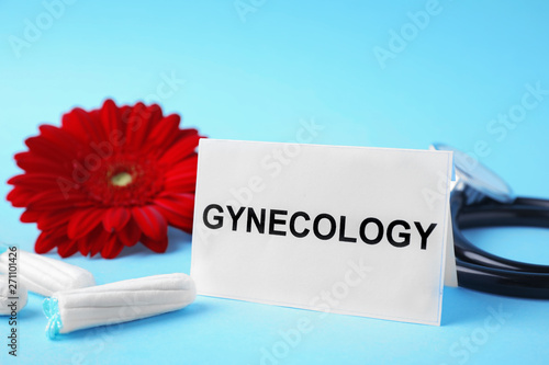 Card with word Gynecology, stethoscope, tampons and flower on color background