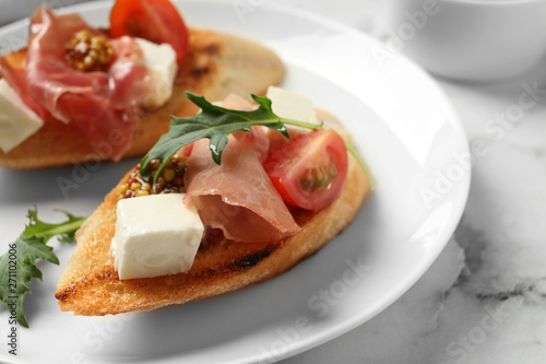 Plate of tasty bruschettas with prosciutto on table, closeup