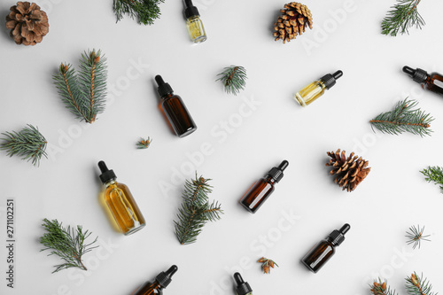 Different little bottles with essential oils among pine branches on white background, flat lay