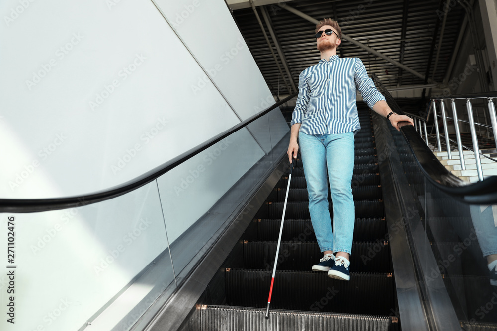 Blind person with long cane on escalator indoors. Space for text