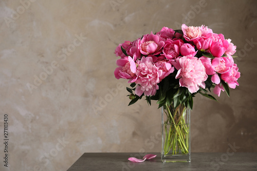 Fototapeta Naklejka Na Ścianę i Meble -  Fragrant peonies in vase on table against color background, space for text. Beautiful spring flowers