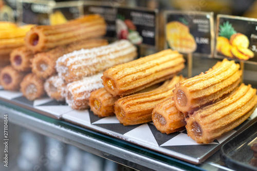 Different types of traditional sweet spanish dessert churros with filling on the market or bakery showcase. Hot baked pastry dish.