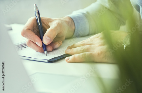 Businessman hand writing note on a notebook. Business man working at office desk. Close up of empty notebook on a blackboard with office supplies.