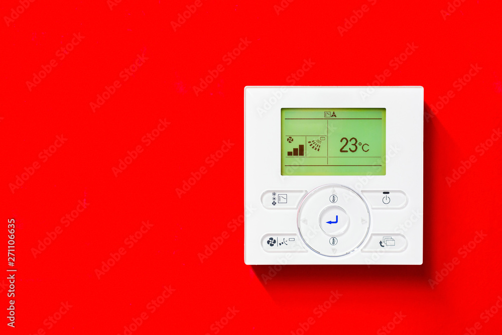 Close up of the white colored AC control unit with a green backlit display that shows the values and analogous buttons, with symbols, which serve to control. Placed on a red wall in the background. Close up of the white colored AC control unit with a green backlit display that shows the values and analogous buttons, with symbols, which serve to control. Placed on a red wall in the background.