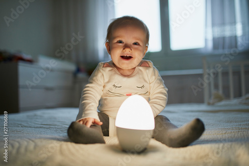 Canvas Print Adorable baby girl playing with bedside lamp in nursery