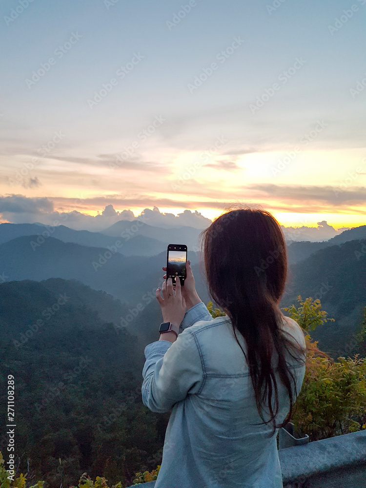 a girl takes a picture of a sunset on her phone