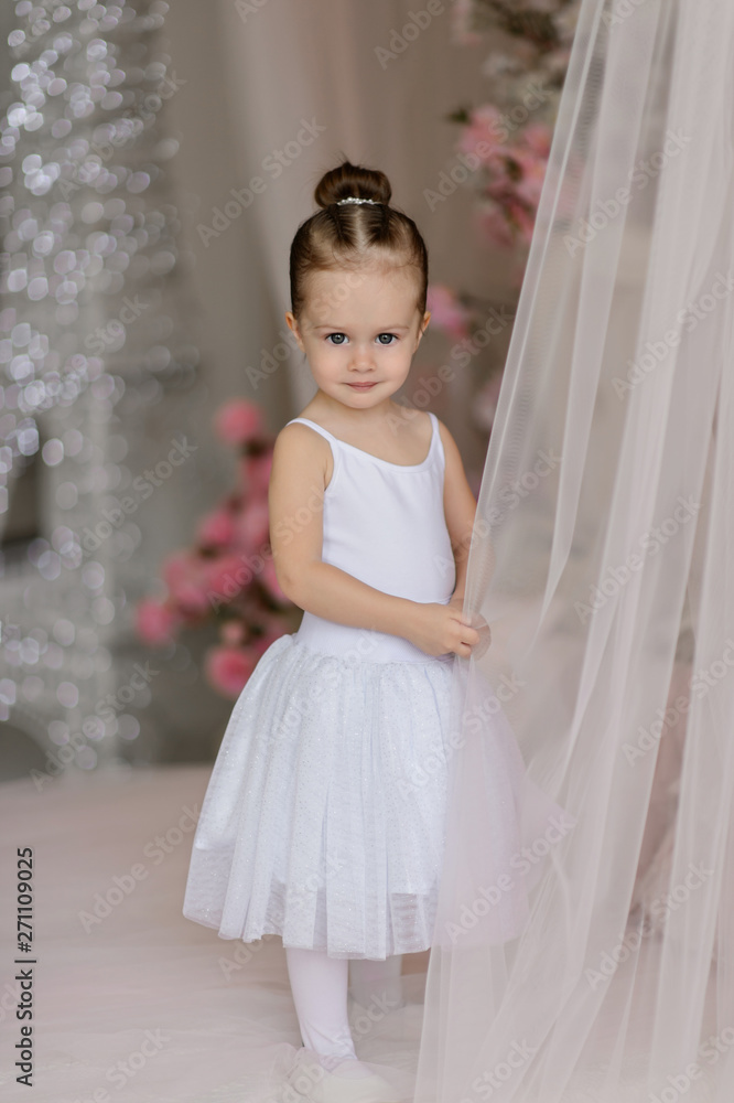 Beautiful small girl in white dress posing indoor.