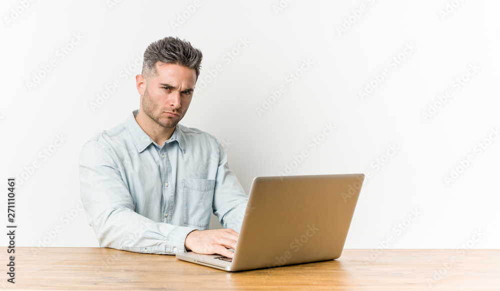 Young handsome man working with his laptop frowning face in displeasure, keeps arms folded. Young handsome man working with his laptop frowning face in displeasure, keeps arms folded.