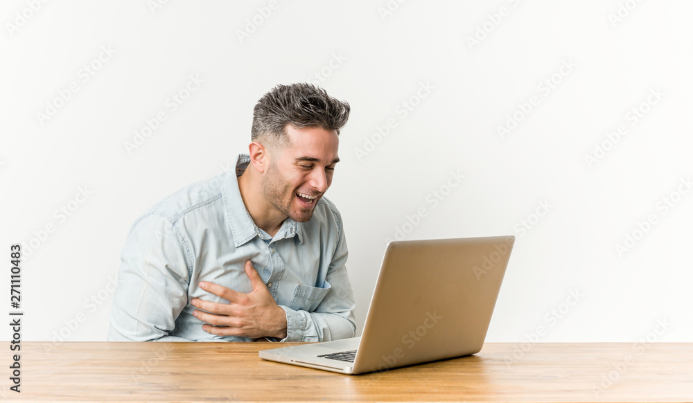 Young handsome man working with his laptop laughs happily and has fun keeping hands on stomach. Young handsome man working with his laptop laughs happily and has fun keeping hands on stomach.