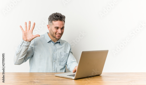 Young handsome man working with his laptop smiling cheerful showing number five with fingers.