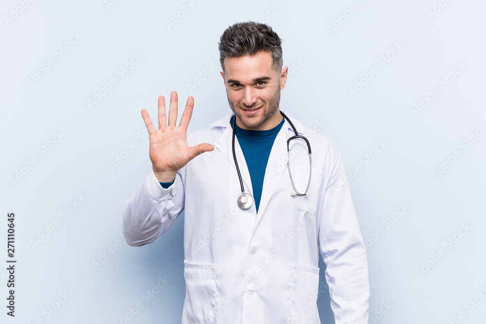 Young handsome doctor man smiling cheerful showing number five with fingers. Young handsome doctor man smiling cheerful showing number five with fingers.
