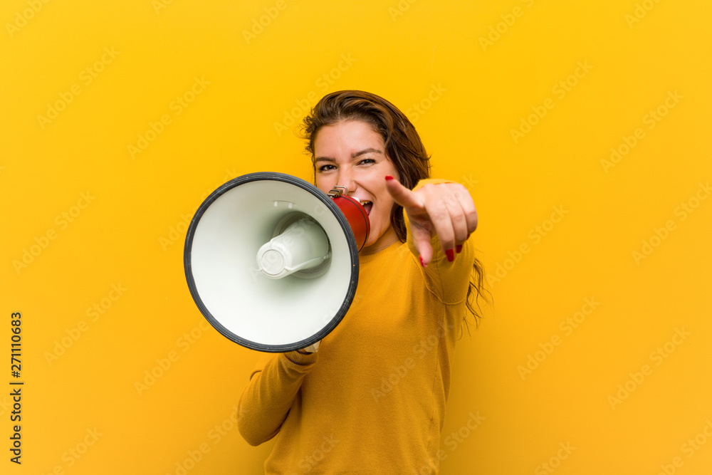 Young european woman holding a megaphone cheerful smiles pointing to front. - obrazy, fototapety, plakaty 