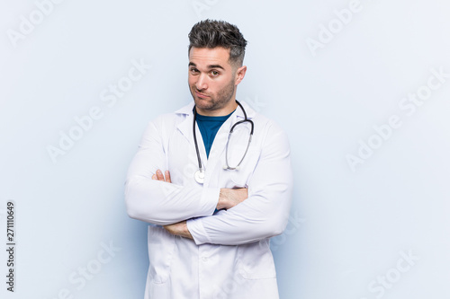 Young handsome doctor man unhappy looking in camera with sarcastic expression.