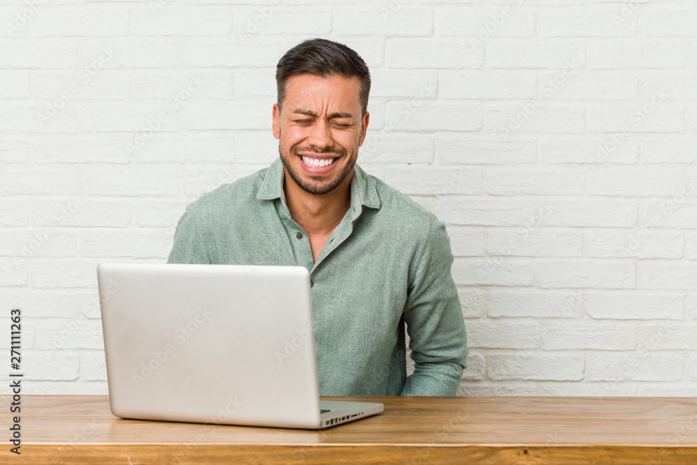 Young filipino man sitting working with his laptop laughs and closes eyes, feels relaxed and happy. Young filipino man sitting working with his laptop laughs and closes eyes, feels relaxed and happy.