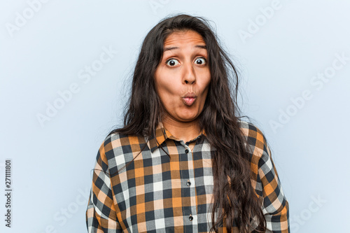 Young cool indian woman shrugs shoulders and open eyes confused.