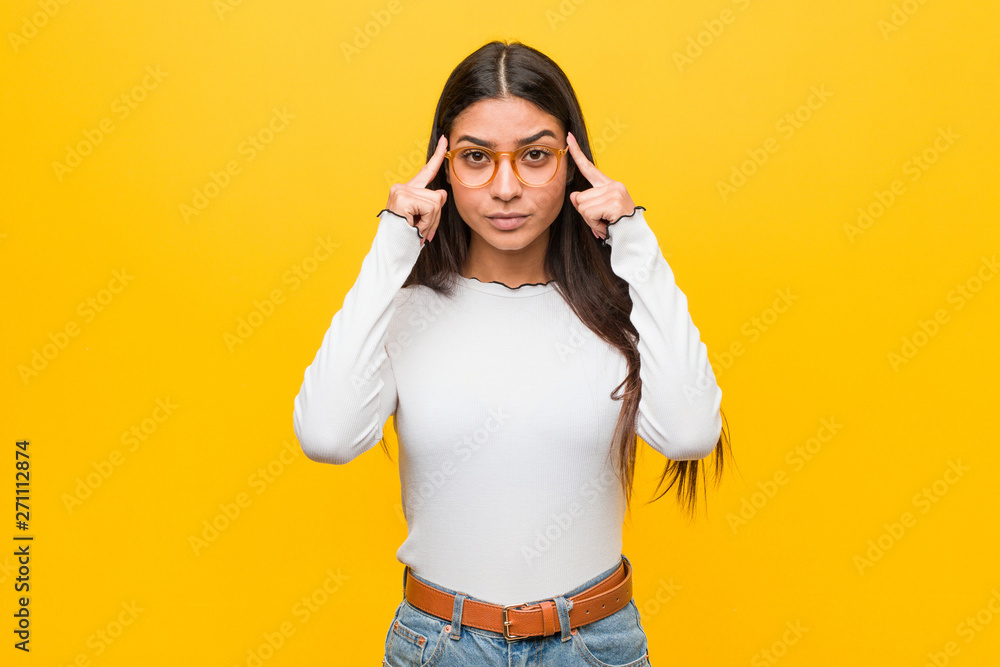 Young pretty arab woman against a yellow background focused on a task, keeping forefingers pointing head. - obrazy, fototapety, plakaty 