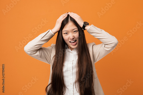 Young business chinese woman laughs joyfully keeping hands on head. Happiness concept. © Asier