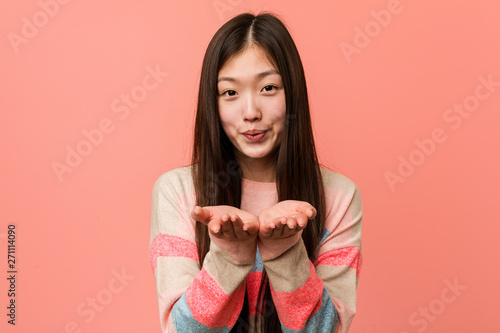 Young cool chinese woman folding lips and holding palms to send air kiss.