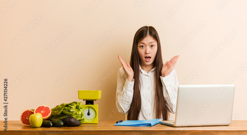 Young nutritionist chinese woman working with her laptop surprised and shocked. Young nutritionist chinese woman working with her laptop surprised and shocked.
