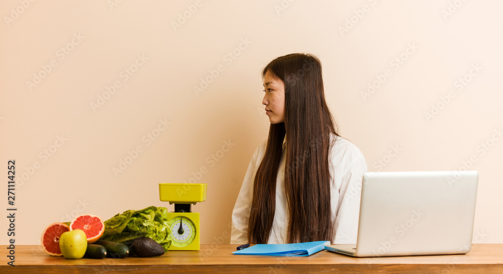 Young nutritionist chinese woman working with her laptop gazing left, sideways pose. Young nutritionist chinese woman working with her laptop gazing left, sideways pose.