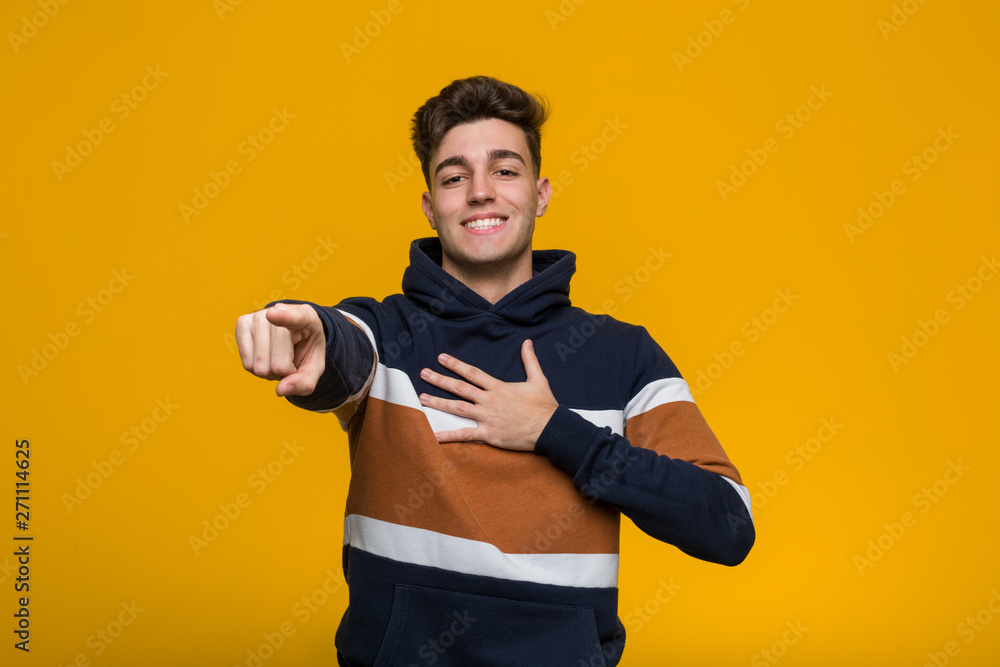 Young cool man wearing a hoodie points with thumb finger away, laughing and carefree. Young cool man wearing a hoodie points with thumb finger away, laughing and carefree.