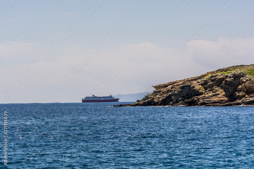 A ferry boat passing behind a rock as seen from the beach in the island of Andros, Cyclades, Greece