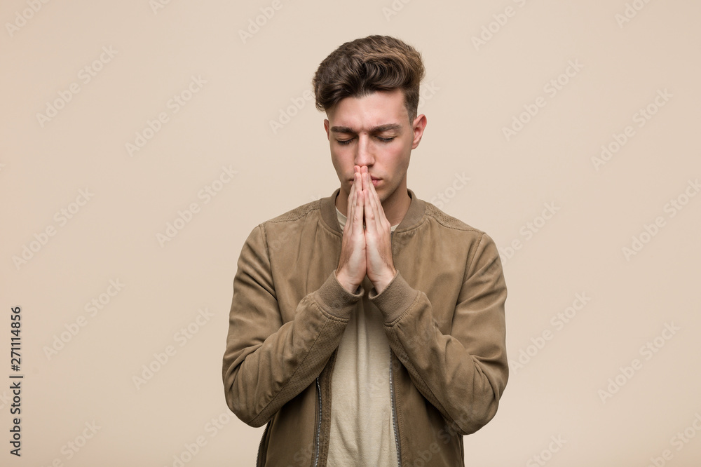 Young caucasian man wearing a brown jacket holding hands in pray near mouth, feels confident. Young caucasian man wearing a brown jacket holding hands in pray near mouth, feels confident.