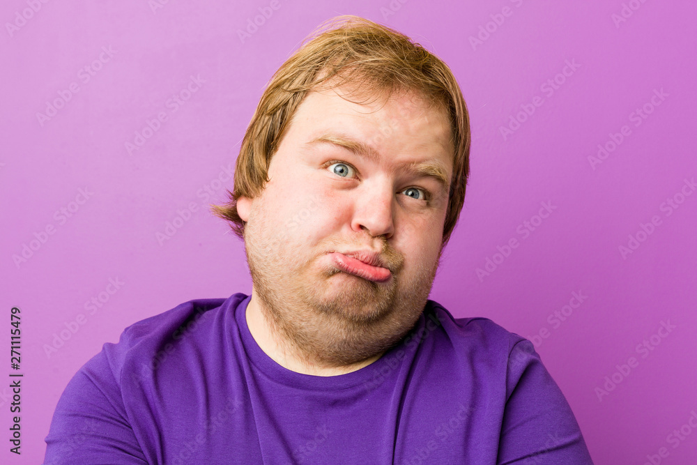 Fototapeta premium Young authentic redhead fat man blows cheeks, has tired expression. Facial expression concept.