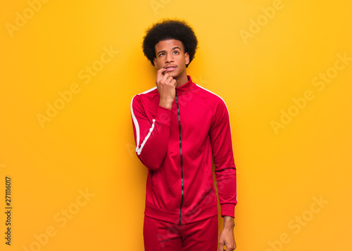 Young sport black man over an orange wall doubting and confused