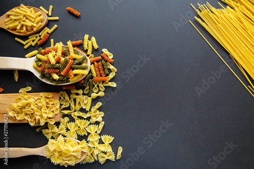 Flat lay of macaroni. Different kinds of spaghetti on the black background. Macaroni isolated on the black background. Black background in sunlight. Cuisine concept. 