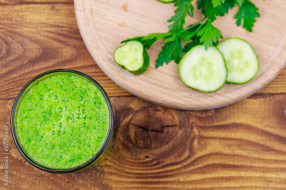 Glass of green detox smoothie of cucumber and parsley on a wooden table. Top view Glass of green detox smoothie of cucumber and parsley on a wooden table. Top view