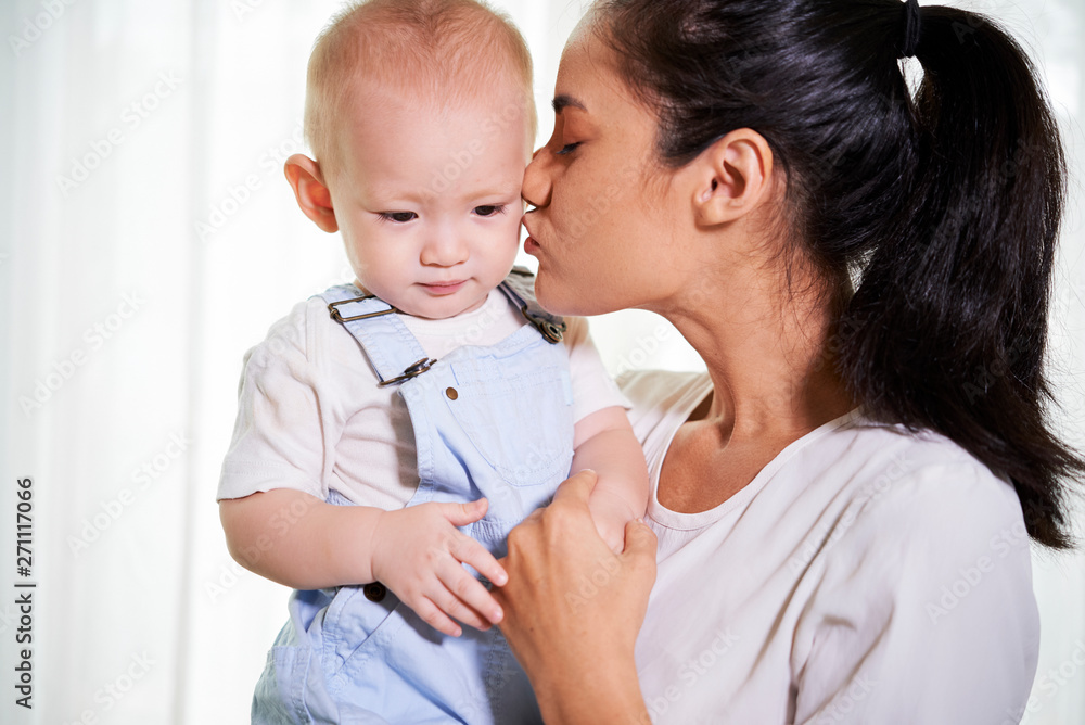 Cheerful young woman kissing her little son on cheek Cheerful young woman kissing her little son on cheek