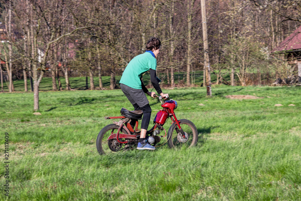 Teenager frolic on old-fashioned red motorbike in the field. Young boy enjoy rides on motorcycles. Jawa 50 pioneer. Riding a motorcycle in stand position. Fichtl. Fechtl. Pincek. Teenager frolic on old-fashioned red motorbike in the field. Young boy enjoy rides on motorcycles. Jawa 50 pioneer. Riding a motorcycle in stand position. Fichtl. Fechtl. Pincek.