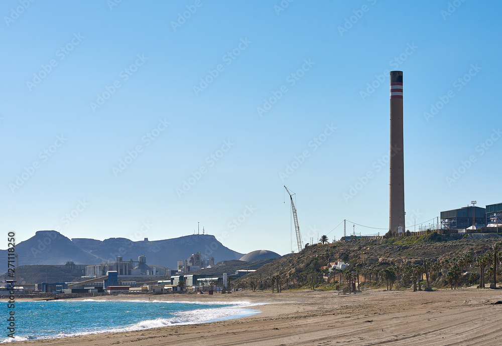 Empty sandy beach, Mediterranean Sea bay blue clear sky and chimney of cement factory in Carboneras. Province of Almeria. Spain