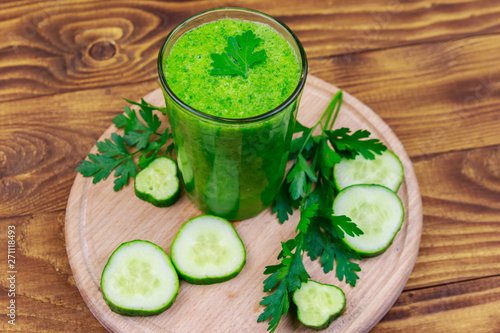 Glass of green detox smoothie of cucumber and parsley on a wooden table