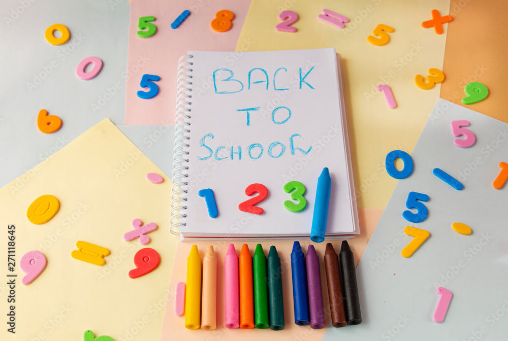 Back to school inscription in blue in a notebook, numbers and pencils on a colorful background top view Back to school inscription in blue in a notebook, numbers and pencils on a colorful background top view