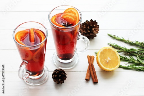 Two glasses of hot red mulled wine or gluhwein with orange, cinnamon sticks on light background. Spicy warm beverage. Seasonal mulled drink.