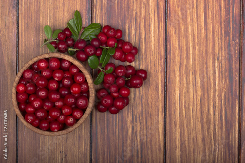 cowberries with leaves and wooden cup on wooden background
